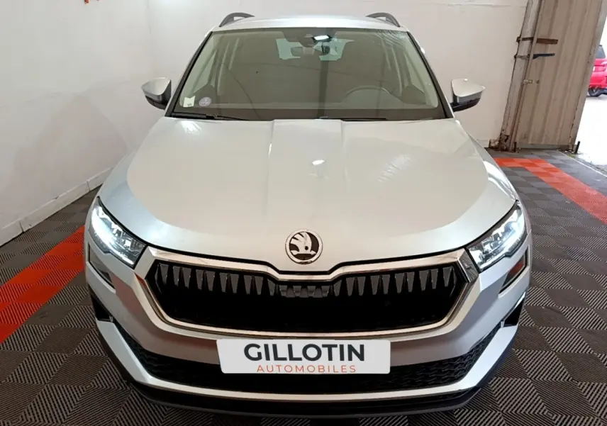 Vue frontale d'un Skoda Karoq gris clair avec calandre noire distinctive et phares LED allumés.