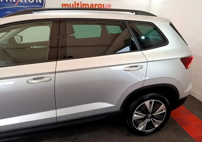 Vue latérale droite d'un SKODA KAROQ gris clair, mettant en valeur les jantes alliage et les vitres teintées.