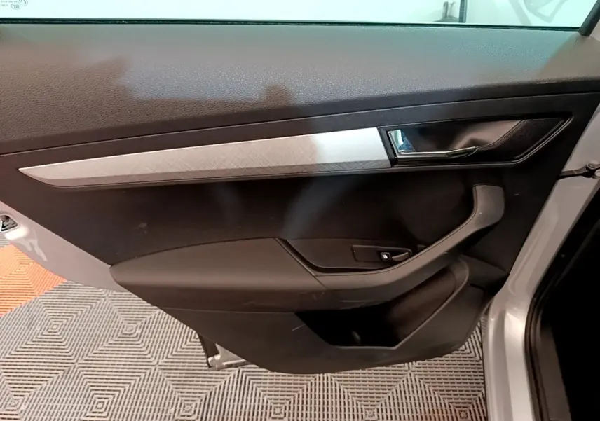 Vue intérieure côté gauche de la porte avant gris clair du Skoda Karoq avec poignée et commande de fenêtre intégrée.