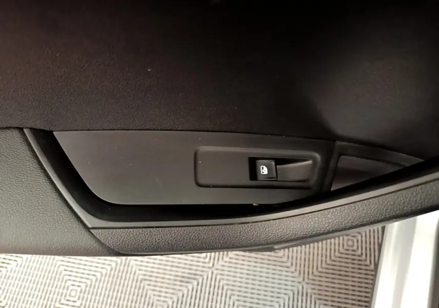 Gros plan sur le bouton de verrouillage des portes sur la portière intérieure noire d’un Skoda Karoq gris clair.
