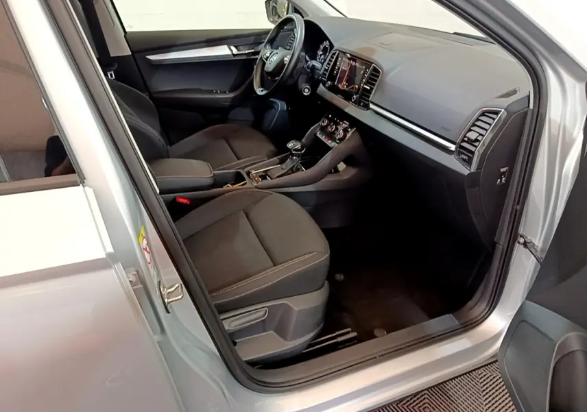 Vue intérieure côté conducteur d'un Skoda Karoq gris clair, montrant sièges noirs et tableau de bord avec écran tactile.