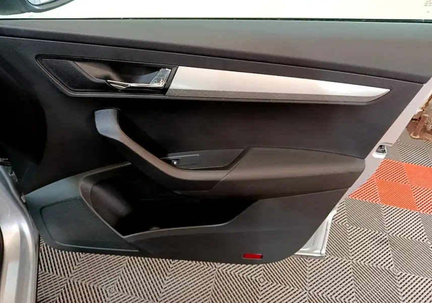 Vue intérieure de la porte avant gauche d’un Skoda Karoq gris clair, avec garniture noire et insert argenté.