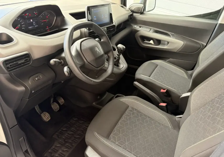 Vue intérieure côté conducteur du Peugeot Rifter blanc 2021, montrant le volant, tableau de bord et sièges tissu gris.