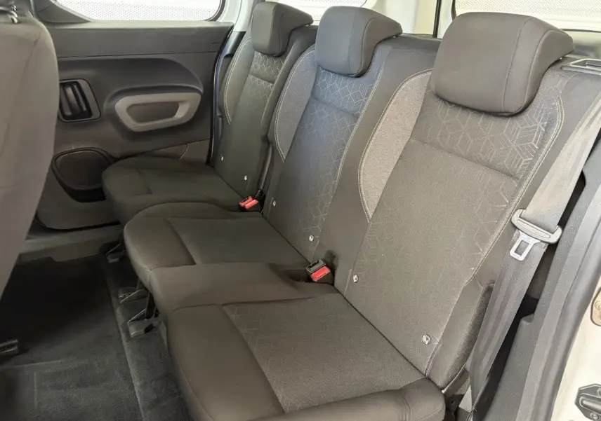 Vue latérale droite sur la banquette arrière noire du Peugeot Rifter blanc, montrant trois sièges avec appuie-têtes.