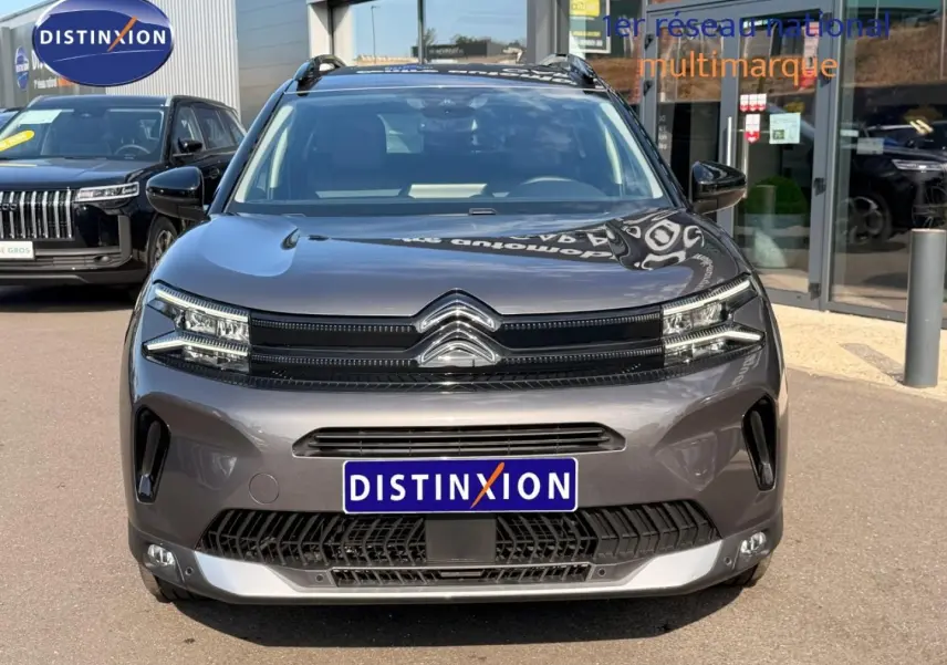 Vue avant d'un Citroën C5 Aircross gris Platinium avec calandre noire et barres de toit visibles.