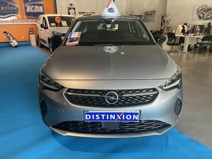 Vue frontale d'une Opel Corsa gris métal exposée en showroom avec plaque Distinxion visible sur un sol bleu.