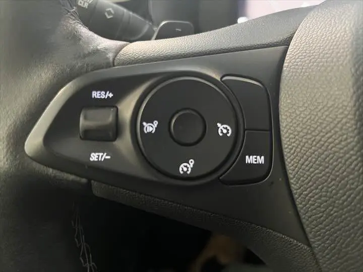Gros plan sur les commandes de régulateur de vitesse au volant cuir noir de l'Opel Corsa gris métal 2021 côté gauche.