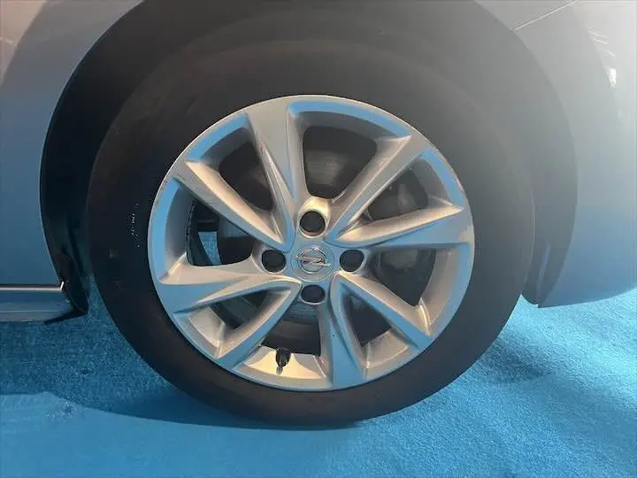 Gros plan sur la jante alliage argentée de l'Opel Corsa gris métal, vue côté gauche sur sol bleu.