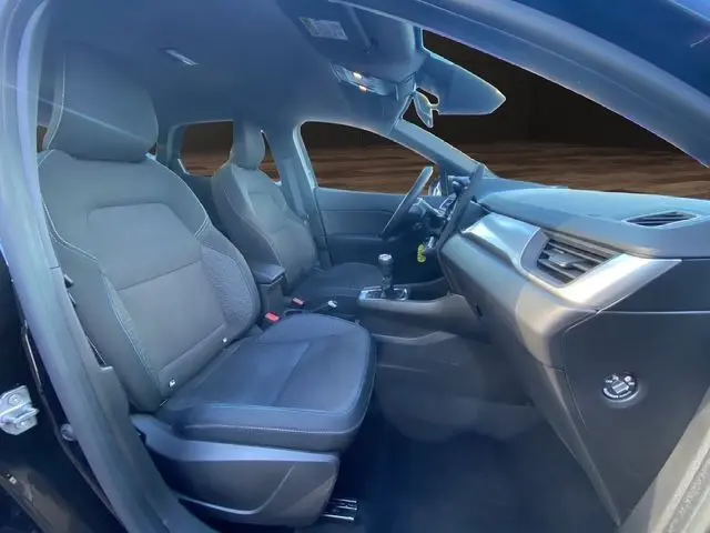 Intérieur noir du Renault Captur 2024 vu de côté gauche, montrant sièges tissu et tableau de bord moderne.