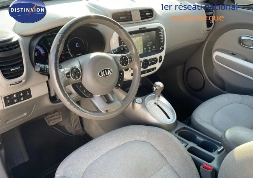 Vue intérieure avant de la Kia Soul EV 2016, montrant le volant, la console centrale avec écran tactile et sièges tissu gris clair.