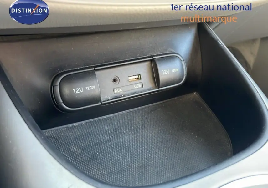 Gros plan sur la console centrale du Kia Soul EV 2016 montrant les prises 12V, USB et AUX dans un intérieur noir.
