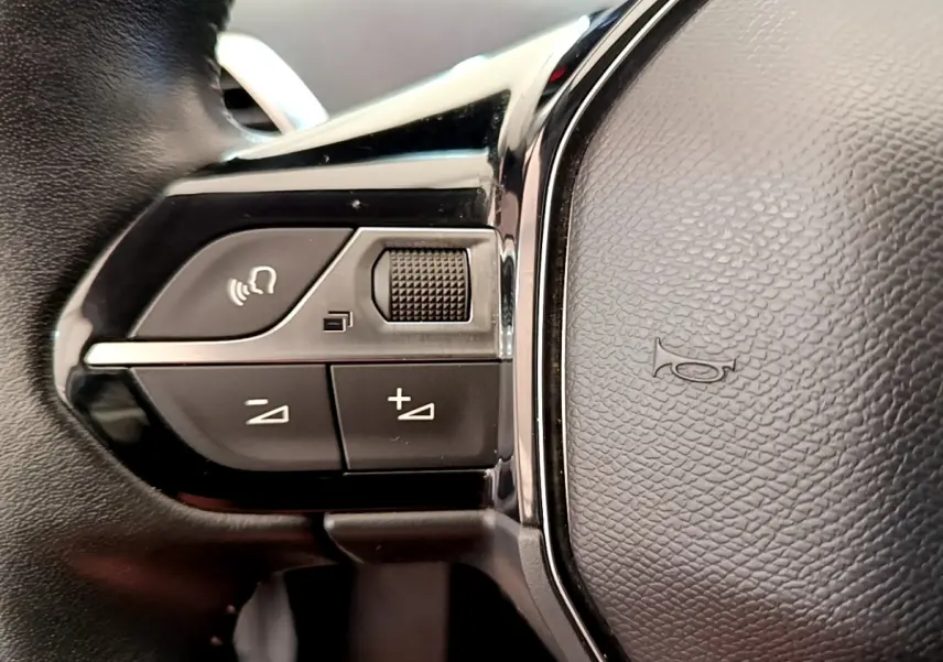 Gros plan sur les commandes gauche du volant cuir noir du Peugeot 3008 gris foncé, avec boutons de volume et commande vocale.