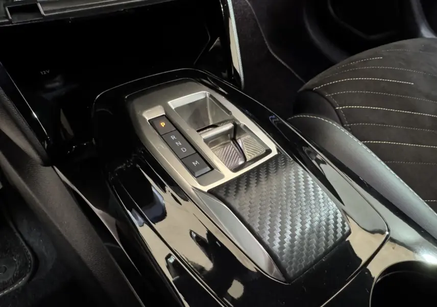Gros plan sur la console centrale noire brillante avec sélecteur de boîte auto et finition carbone dans une Peugeot 208 Hybrid 136 eDCS6 GT.