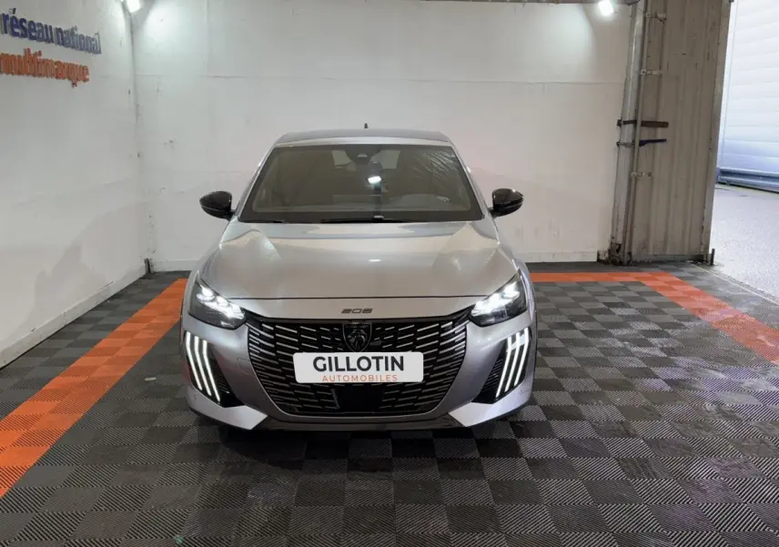 Vue frontale d'une Peugeot 208 Hybrid 136 eDCS6 GT gris clair avec phares LED et calandre noire distinctive.