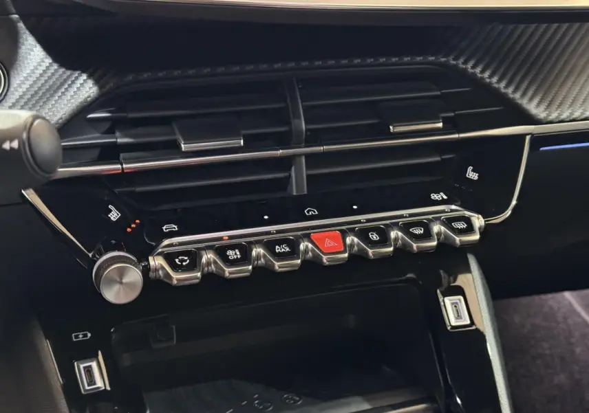 Gros plan sur la console centrale noire brillante de la Peugeot 208 Hybrid 136, avec boutons chromés et écran tactile.