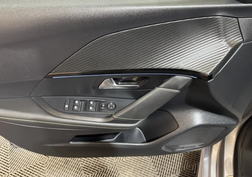 Gros plan sur la porte côté conducteur de la Peugeot 208 Hybrid gris clair, avec insert imitation carbone et commandes électriques.