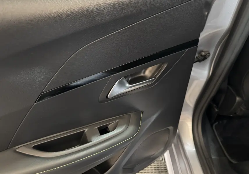 Gros plan sur la porte arrière droite intérieure noire avec surpiqûres vertes et poignée argentée d’une Peugeot 208 gris clair.