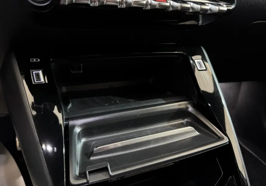 Détail de la console centrale noire de la Peugeot 208 Hybrid 136 eDCS6 GT avec ports USB et rangement ouvert.