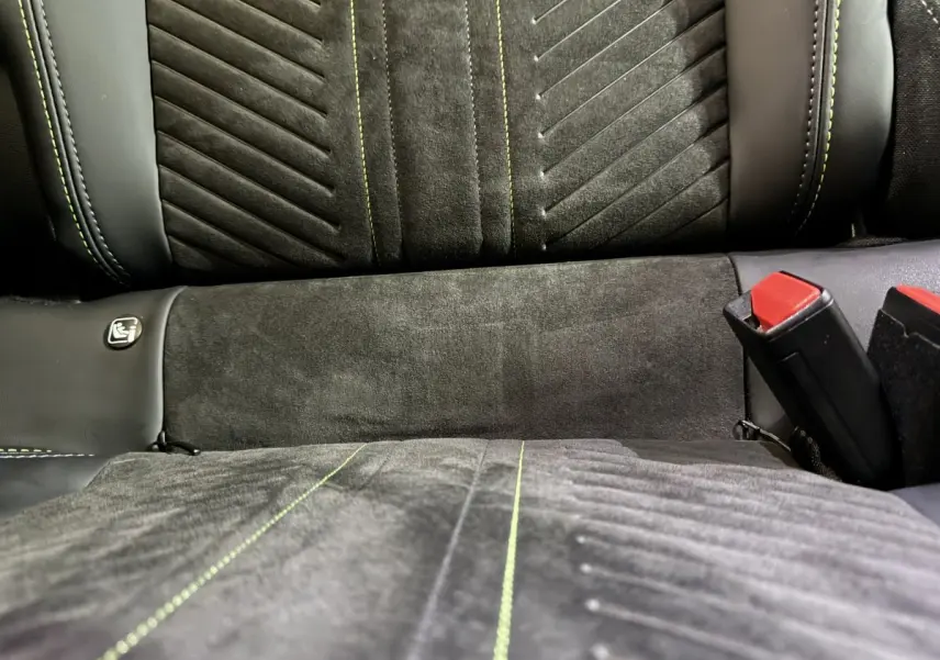 Gros plan sur la banquette arrière grise de la Peugeot 208 Hybrid 136 eDCS6 GT avec surpiqûres vertes et ceintures rouges.