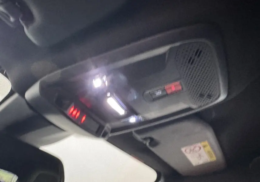 Vue intérieure du plafond avant de la Peugeot 208 Hybrid gris clair, montrant les éclairages et commandes intégrés.