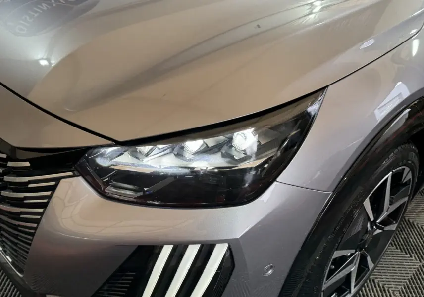 Gros plan sur l'avant droit gris clair du Peugeot 208 Hybrid 136 eDCS6 GT, avec phares LED et jante noire design.