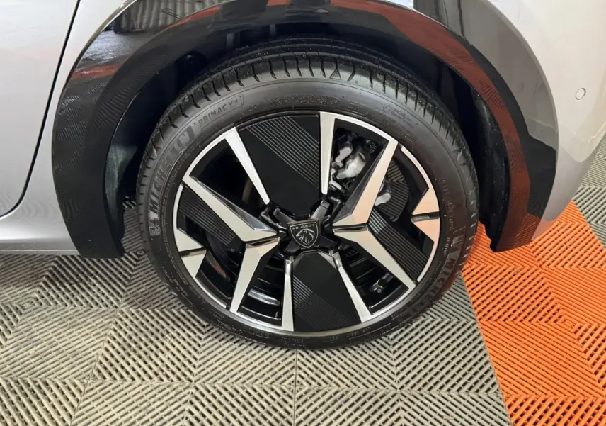 Gros plan sur la roue avant droite de la Peugeot 208 Hybrid gris clair avec jante alliage noire et argentée design moderne.