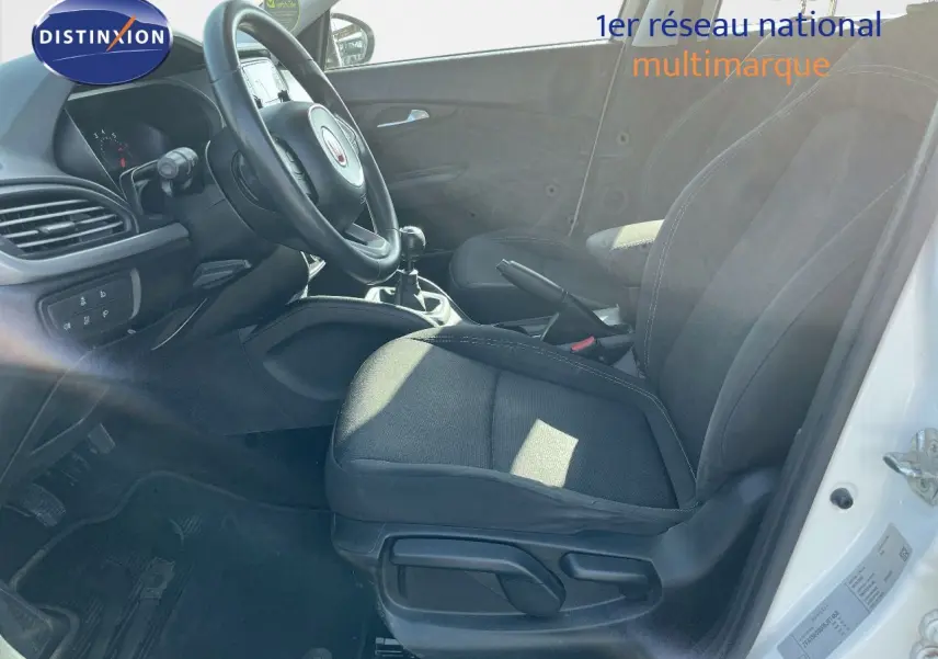 Vue intérieure côté conducteur d'une Fiat Tipo blanche 2018, montrant les sièges noirs et la boîte manuelle.