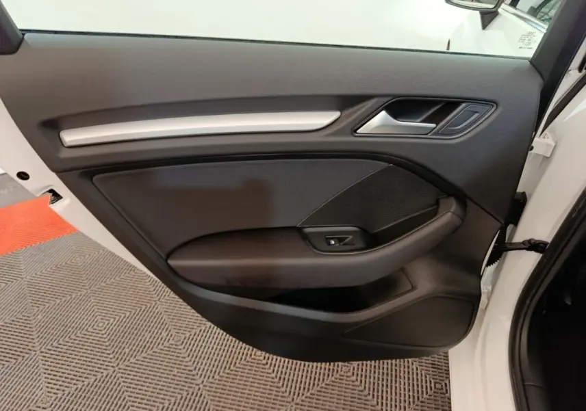 Vue rapprochée de la porte avant droite d’une Audi A3 blanche, montrant la garniture intérieure noire avec poignée et commande de vitre.