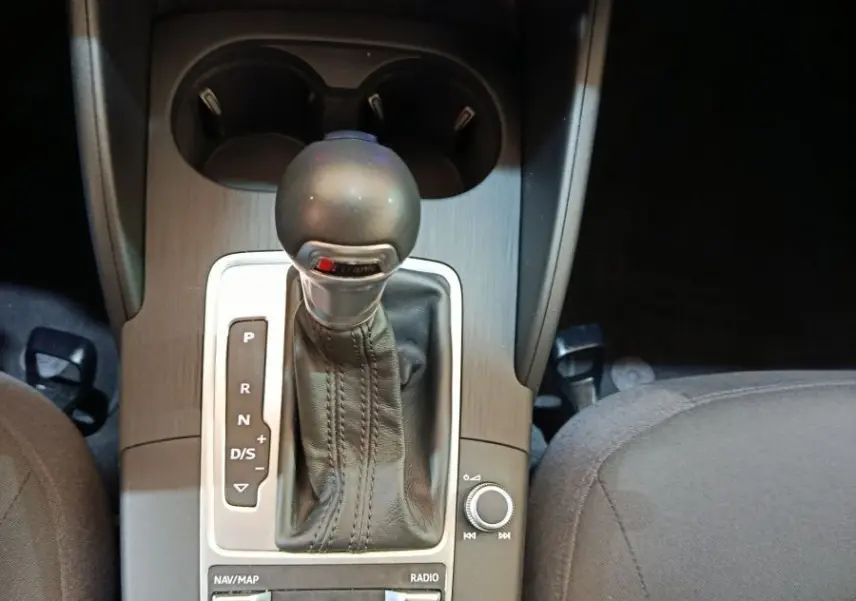 Vue rapprochée de la console centrale de l'Audi A3 blanche, mettant en valeur le levier de vitesse automatique et les commandes de climatisation.