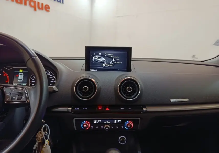 Vue intérieure du tableau de bord d'une Audi A3 35 TDI blanc, avec écran tactile central et commandes de climatisation digitales.