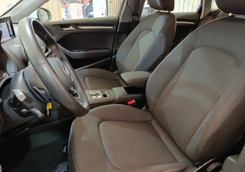 Vue intérieure côté conducteur de l'Audi A3 35 TDI 150 S tronic Business Line avec sièges tissu gris et volant cuir multifonctions.