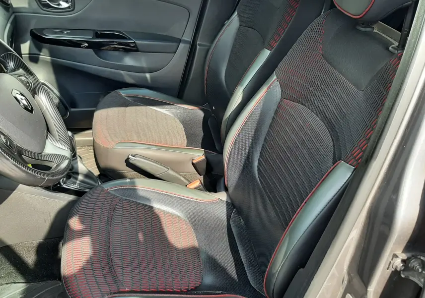 Vue intérieure côté conducteur du Renault Captur 2016, sièges noirs avec surpiqûres rouges et volant cuir.
