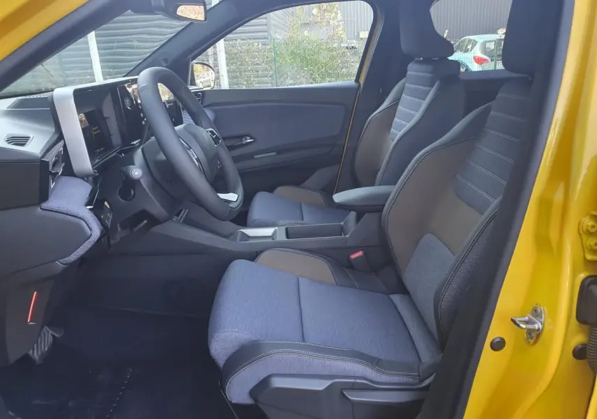 Vue intérieure côté conducteur de la Renault R5 E-Tech jaune pop, montrant sièges bi-matière et tableau de bord moderne.