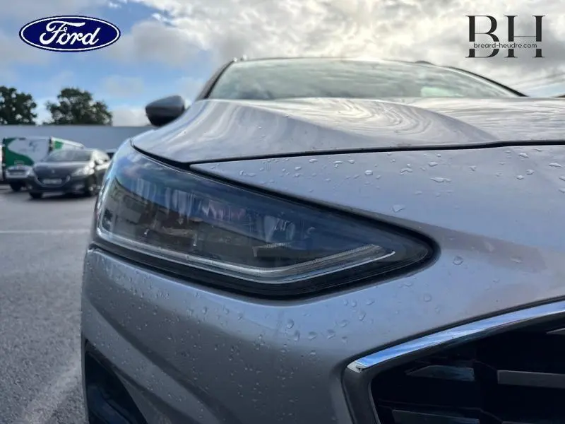 Gros plan sur le phare avant gauche d'une Ford Focus SW 2023 gris lunaire métallisé avec gouttes d'eau visibles.