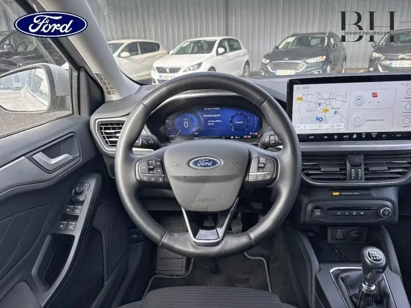 Vue intérieure du poste de conduite de la Ford Focus SW 2023, volant cuir multifonction et écran tactile GPS.