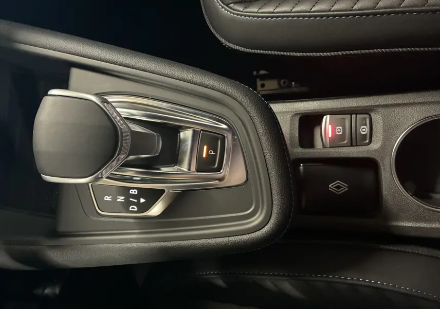 Vue rapprochée de la console centrale du Renault Captur E-Tech hybride 2025, avec levier de vitesse automatique et bouton de frein à main électronique.