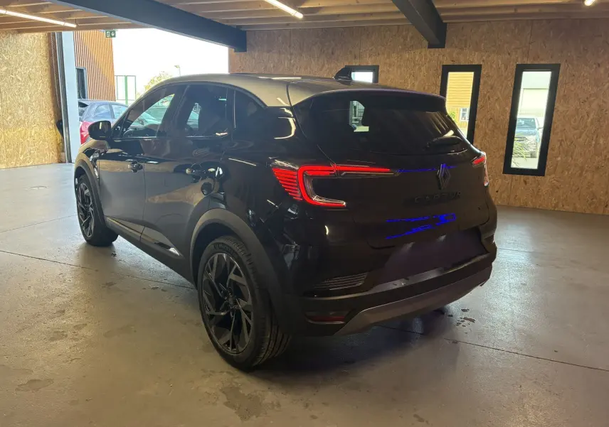 Vue 3/4 arrière droite du Renault Captur E-Tech Full Hybrid noir étoile avec toit gris, en intérieur, feux arrière allumés.