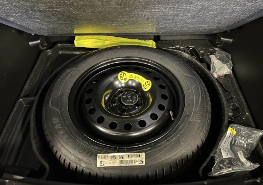 Gros plan sur la roue de secours noire dans le coffre du Jeep Compass 2024, entourée d’accessoires de bord.