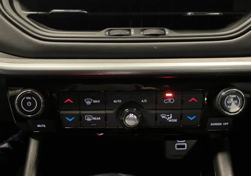 Gros plan sur la console centrale noire du Jeep Compass 2024, avec commandes climatisation et audio éclairées.