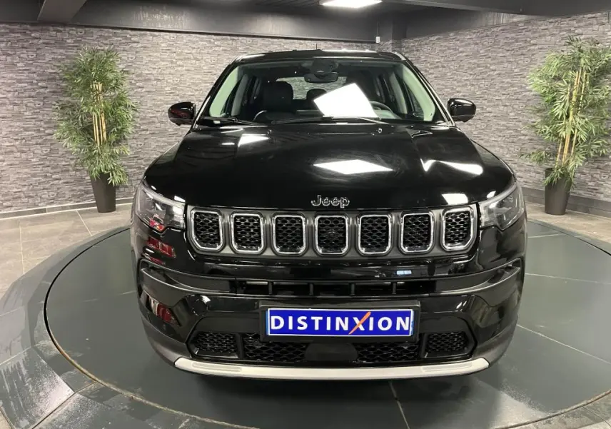 Vue frontale d'un Jeep Compass noir 2024 avec calandre chromée et plaque Distinxion dans un showroom.