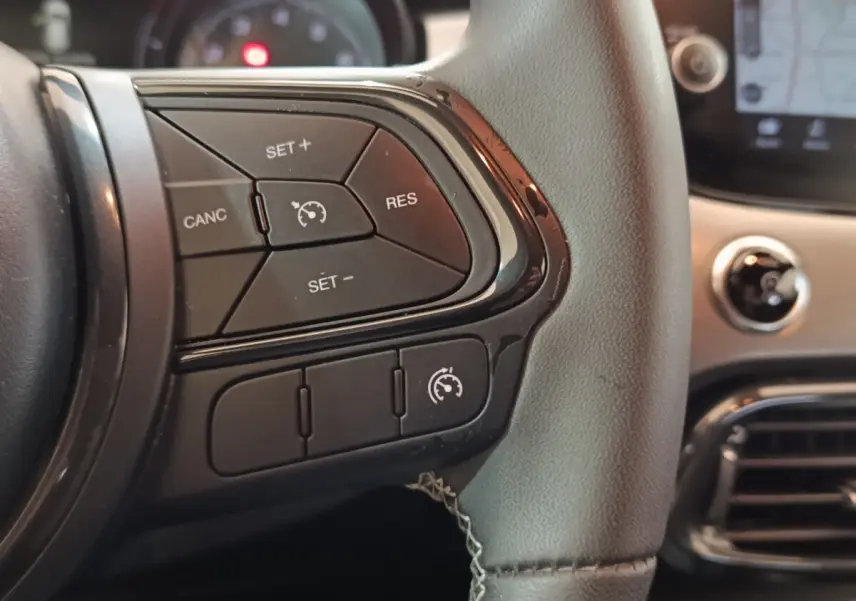 Gros plan sur les commandes de régulateur de vitesse à gauche du volant d’un Fiat 500X noir, intérieur moderne.