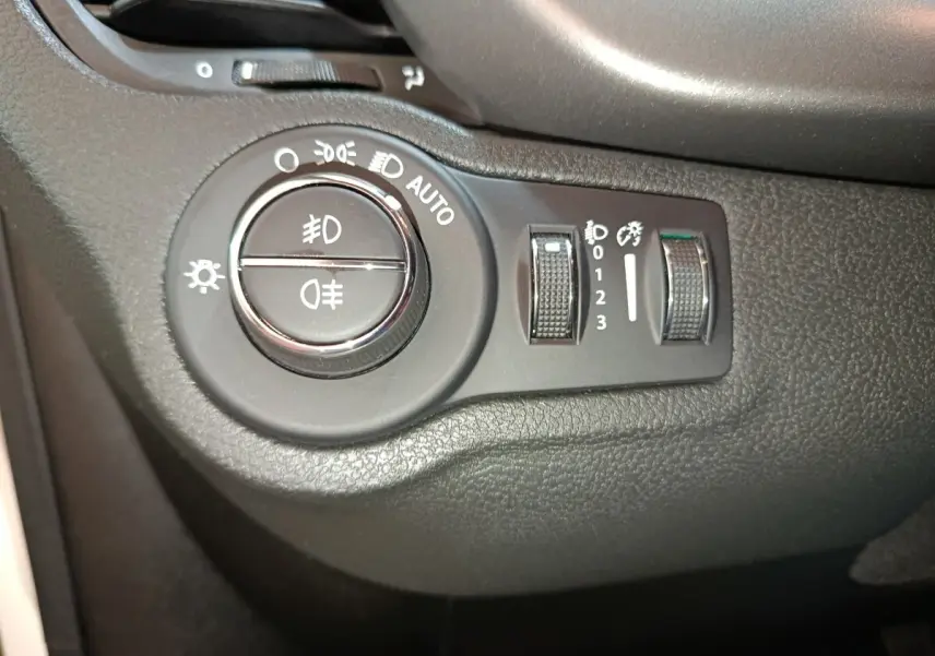 Gros plan sur la commande des phares et réglages d’éclairage à gauche du tableau de bord d’une Fiat 500X noire.