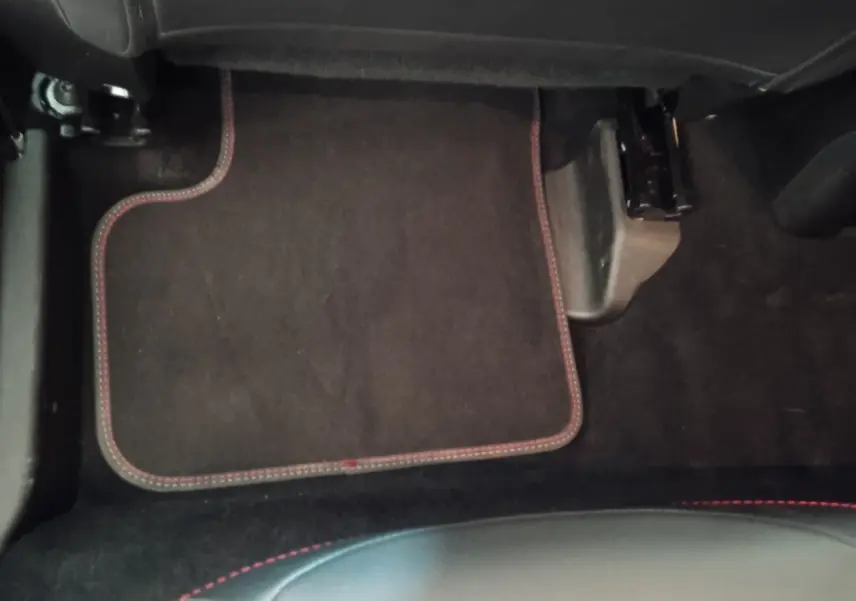 Vue intérieure du plancher côté passager avant de la FIAT 500X noire avec tapis de sol noir et surpiqûres rouges.