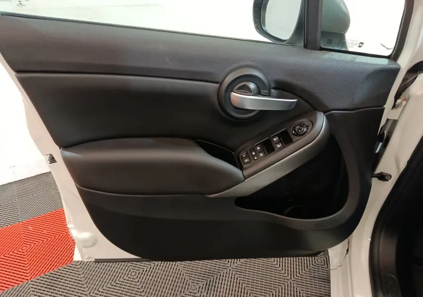 Vue intérieure côté gauche de la porte avant d'une FIAT 500X noire, avec commandes de vitres et poignée argentée.
