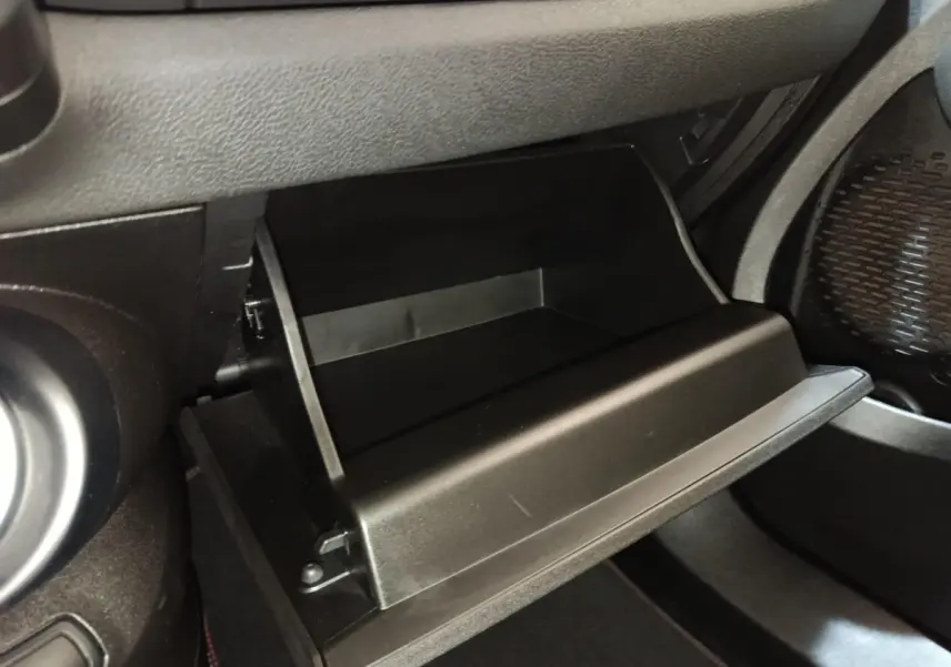 Vue rapprochée de la boîte à gants noire ouverte côté passager dans l’habitacle d’une Fiat 500X noire.