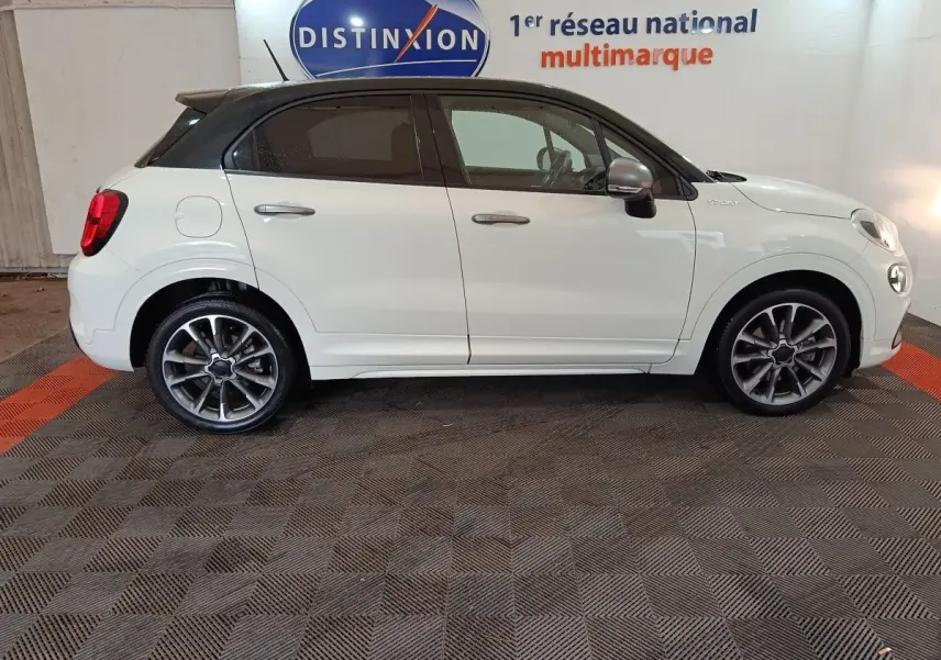 Vue de profil côté gauche d'une FIAT 500X blanche avec toit noir et jantes alliage sport dans un showroom.