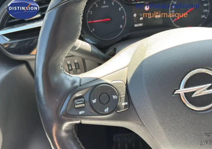 Gros plan sur le volant en cuir noir avec commandes intégrées et logo Opel, tableau de bord partiellement visible.