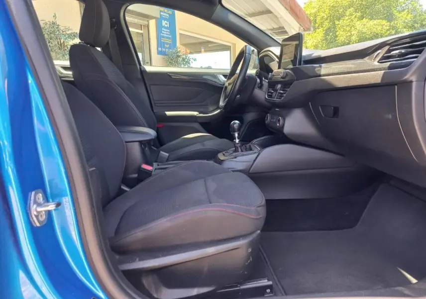 Vue intérieure côté conducteur de la Ford Focus bleu 2019, avec sièges noirs et levier de vitesse manuel visible.