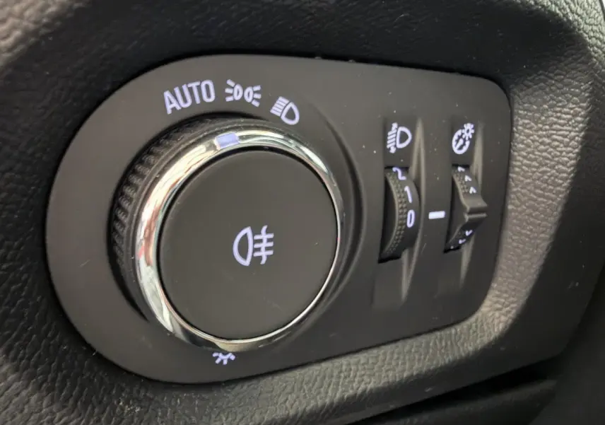 Gros plan sur la molette de réglage des phares d’un Opel Corsa gris clair, avec commandes d’éclairage et réglages associés.