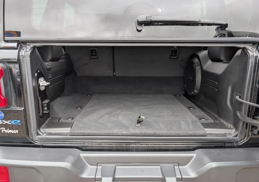 Coffre ouvert d’un Jeep Wrangler 2024 noir, montrant l’espace de rangement intérieur et la roue de secours souple.